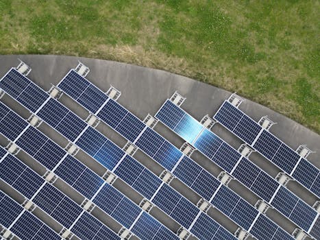 Top-down view of solar panels arranged on a green field, highlighting renewable energy.